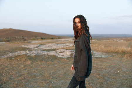 Serene woman in black sweater standing in vast open field with majestic mountain backdropの写真素材