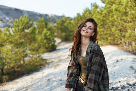 Woman in plaid shirt and jeans standing confidently on hill in serene forest settingの写真素材