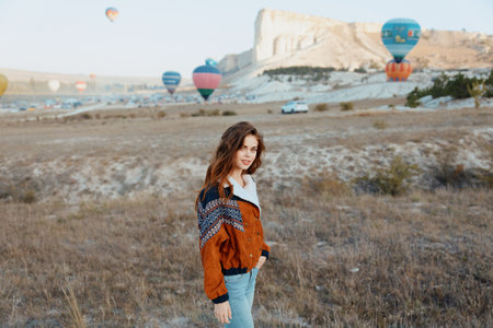 Woman standing in vast field as colorful hot air balloons soar in the sky behind herの写真素材