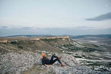 serene sunset woman contemplating valley and mountains from rock perchの写真素材