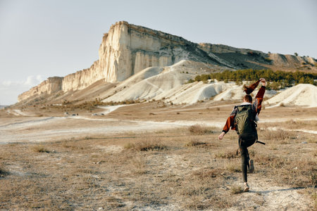 Solitary hiker standing in vast field with majestic mountain backdrop on a sunny dayの写真素材