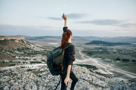 Triumphant woman on mountain peak with backpack reaches up to the sky in celebration of her achievementの写真素材