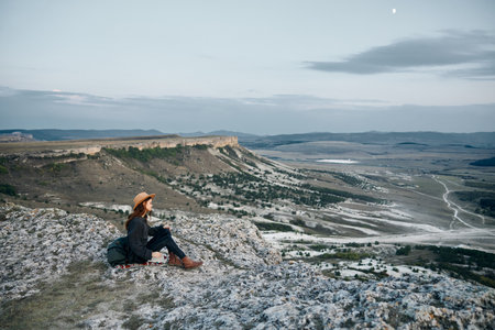 serene woman gazes at moonlit valley from rocky perch at twilightの写真素材