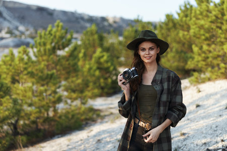 Woman in plaid shirt and hat capturing scenic hillside view with camera on sunny day