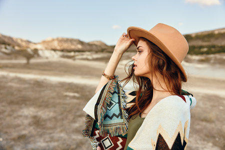 woman in stylish hat and scarf poses in desert landscape with majestic mountains in backgroundの写真素材