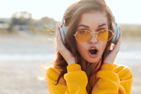 Woman in yellow sweater and sunglasses listening to music with mouth open in joyful expressionの写真素材