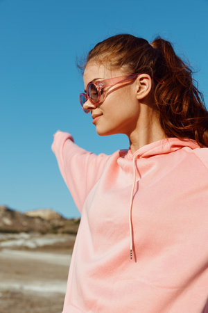 carefree woman in pink sweatshirt and sunglasses enjoying the beach with arms outstretchedの写真素材