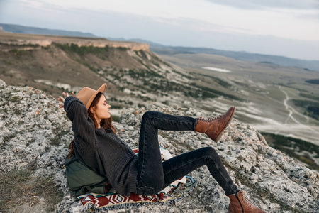 Serene woman resting on rock with legs crossed and feet on blanket in peaceful outdoor settingの写真素材