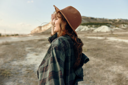 Woman in plaid shirt and hat standing confidently in the vast open field on a sunny day
