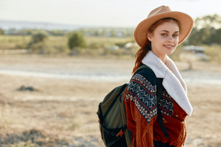 adventurous woman standing in vast field at sunset with backpack and hat