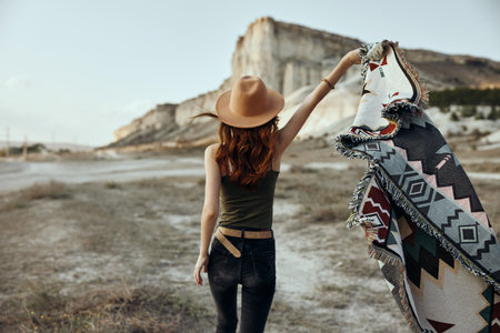Cowgirl in a cowboy hat holding a blanket with mountain range backdrop in the backgroundの写真素材