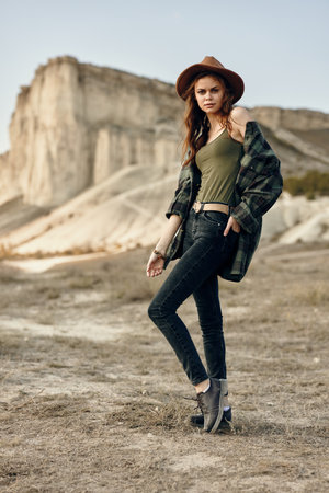 Beautiful woman standing in a sunlit field wearing a stylish hat and green shirt amid nature's beautyの写真素材