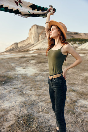 Stylish woman wearing jeans and a hat poses in the desert with a scarf fluttering in the windの写真素材