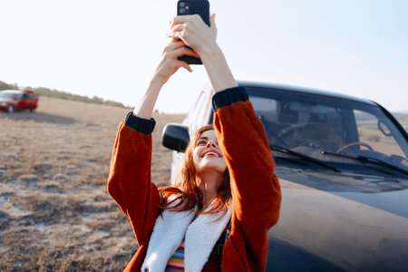 Young woman taking a selfie next to a vintage car in a picturesque field settingの写真素材
