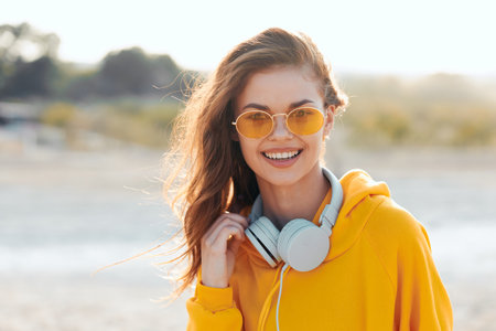 Happy woman in yellow hoodie and sunglasses listening to music on headphones
