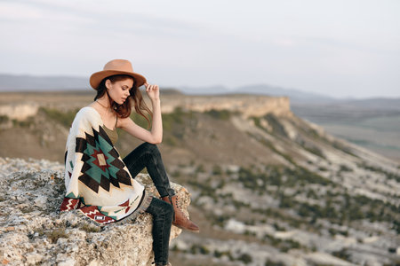 serene woman in hat and blanket gazes confidently at camera from mountain summitの写真素材