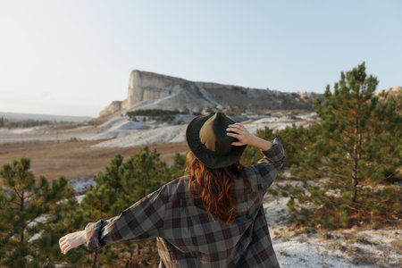 Scenic view woman in plaid shirt and hat on hill overlooking majestic mountain landscapeの写真素材