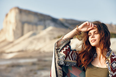 Serene woman in blanket gazes at majestic mountain landscape with hands on head