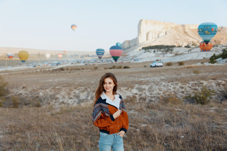 Woman standing in serene field as colorful hot air balloons float in the distanceの写真素材