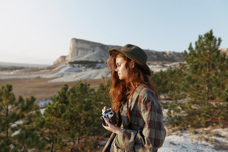 Woman with camera capturing the scenic beauty on a hilltop in plaid shirt and hatの写真素材