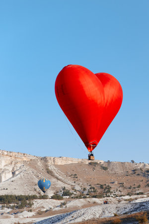 romantic red heart balloon soaring above majestic mountain landscapeの写真素材