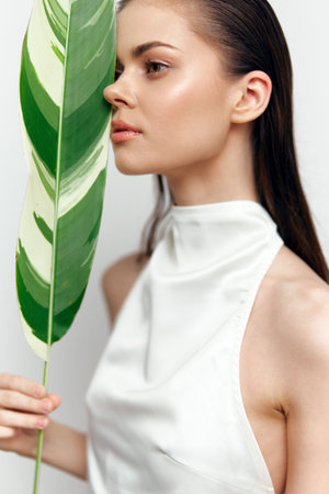 Elegant woman with leaf, showcasing natural beauty and fashion in a minimalist setting, emphasizing green tones and summer vibes.の写真素材