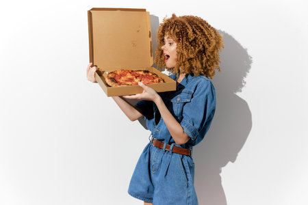 Excited young woman with curly hair holding a pizza box against a white background, celebrating delicious food with vibrant emotions Perfect for food photographyの写真素材