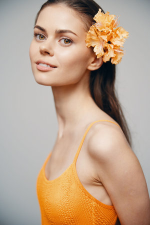 Elegant young model with a flower in her hair, wearing an orange swimsuit, exuding confidence and warmth, perfect for summer themes and swimwear fashion.の写真素材