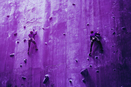Two climbers ascending a purple rock climbing wall, showcasing determination and teamwork, perfect for sports and motivational themesの素材