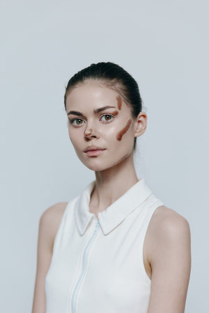 Young woman with artistic face paint in a stylish, sleeveless white top, conveying a modern and creative vibe against a minimalist background.の写真素材