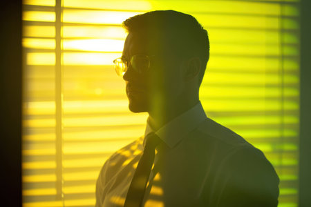 Thoughtful businessman in glasses against yellow striped background, showcasing professionalism and introspection in a contemporary office settingの素材
