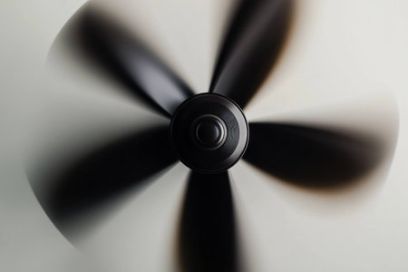 Abstract view of a spinning ceiling fan with blurred motion, showcasing a sleek black design against a neutral background, evoking a sense of coolness and comfortの素材