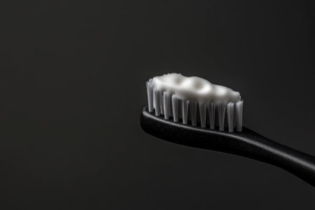Black toothbrush with white foam on bristles against a dark background, symbolizing effective dental hygiene and oral careの素材