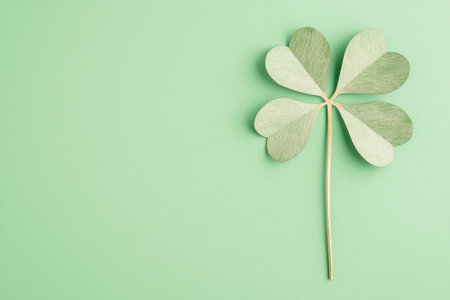 Green paper clover leaf on a light mint background representing good luck and nature, ideal for wellness and eco friendly themesの素材
