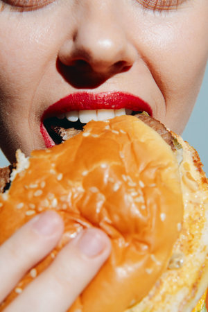 Close-up shot of a woman with red lips biting into a juicy burger, showcasing excitement and indulgence, perfect for food and lifestyle themes.の写真素材