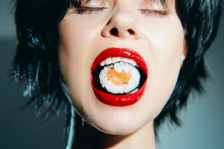 Woman enjoying sushi with red lipstick and closed eyes, highlighting the joyful experience of eating sushi.の写真素材
