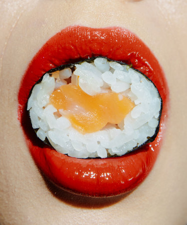 Close-up of vibrant sushi held by a model with red lips, showcasing delicious sushi and playful food art concept. Perfect for culinary and lifestyle themes.の写真素材