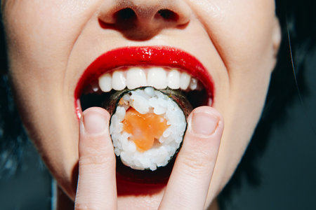 Close-up of a woman holding sushi with red lips and bright smile, showcasing a vibrant sushi...