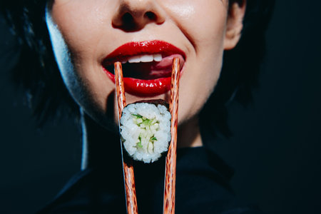 Woman with red lips holding sushi with chopsticks, showcasing vibrant colors and an artistic presentation, ideal for food and lifestyle concepts.の写真素材