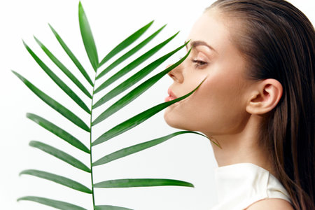 Portrait of a serene model with a palm leaf, showcasing elegance and tranquility in a minimalistic white background. KEYWORDS: model, palm, serenity, elegance, beauty, nature, minimalismの写真素材