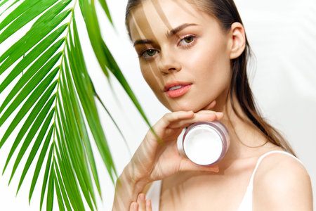 Model displaying skincare product with tropical greenery, showcasing beauty and natural elegance, ideal for skincare promotions.の写真素材