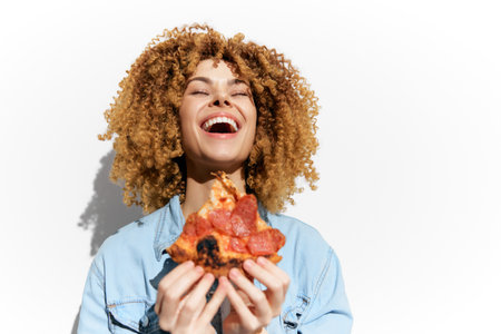 Happy woman enjoying pizza with curly hair on a bright background, conveying joy and a love for food in a casual and vibrant styleの写真素材
