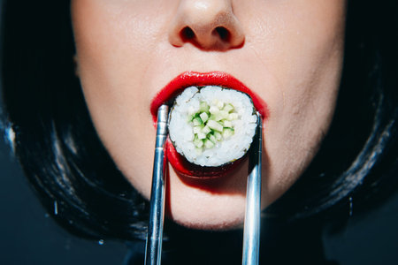 Woman holding sushi with chopsticks, dramatic makeup, and vibrant red lips, showcasing a bold...