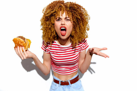 Angry woman with curly hair holding a burger in a striped shirt, expressing frustration Food choice,...