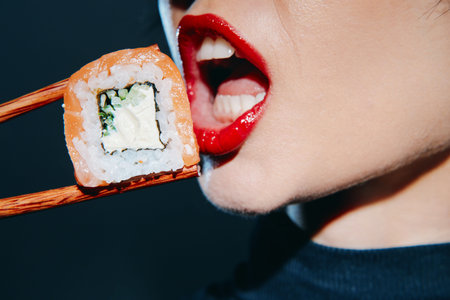 Close-up of a womanâ€™s mouth with bright red lips eating sushi, showcasing a mouthwatering...