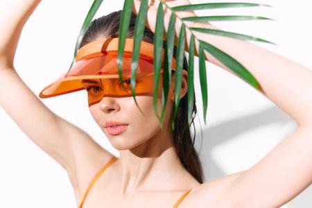Stylish summer portrait of a woman with orange visor and palm leaves, showcasing vibrant fashion and...