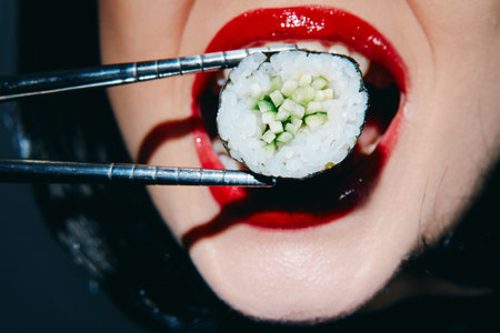 Bold close-up of a model biting sushi with vibrant red lips, showcasing sushi ingredients and modern culinary aesthetics.の写真素材