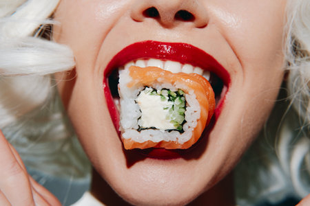 Close-up of a smiling woman with white hair and red lips holding sushi, showcasing vibrant colors and playful emotions in a bright background.の写真素材