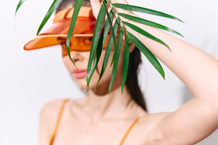 Stylish young woman with orange visor and palm leaves in bright summer fashion. Modern tropical aesthetic for lifestyle photography.の写真素材
