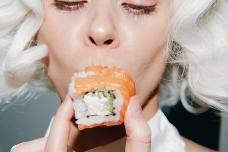 Young woman enjoying sushi with a cheerful expression, showcasing salmon sushi roll against a minimalistic background.の写真素材
